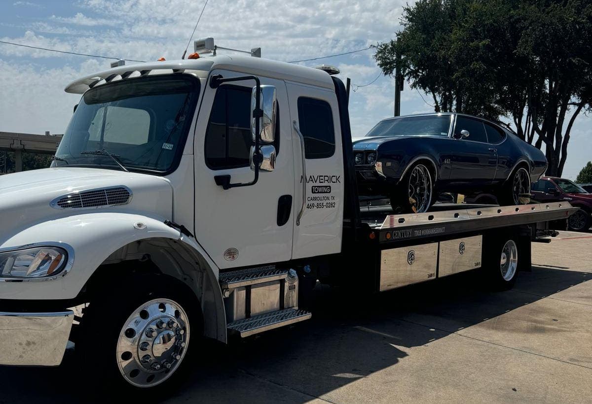 Maverick Towing white flatbed tow truck carrying a dark blue classic Oldsmobile 442 in Dallas