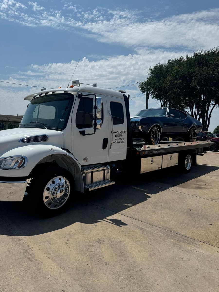 Dark blue classic Oldsmobile 442 on custom wheels secured on a Maverick Towing flatbed