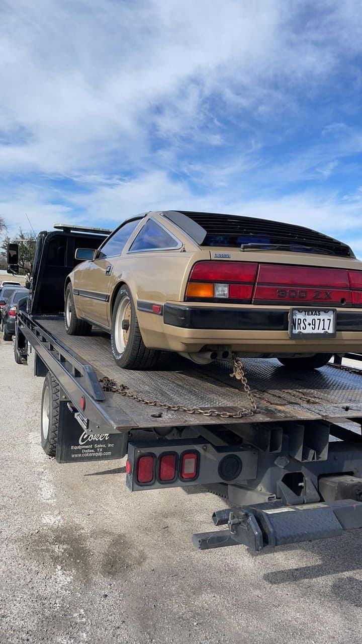 Gold Nissan 300ZX chained to a Maverick Towing flatbed, seen from behind on a clear day