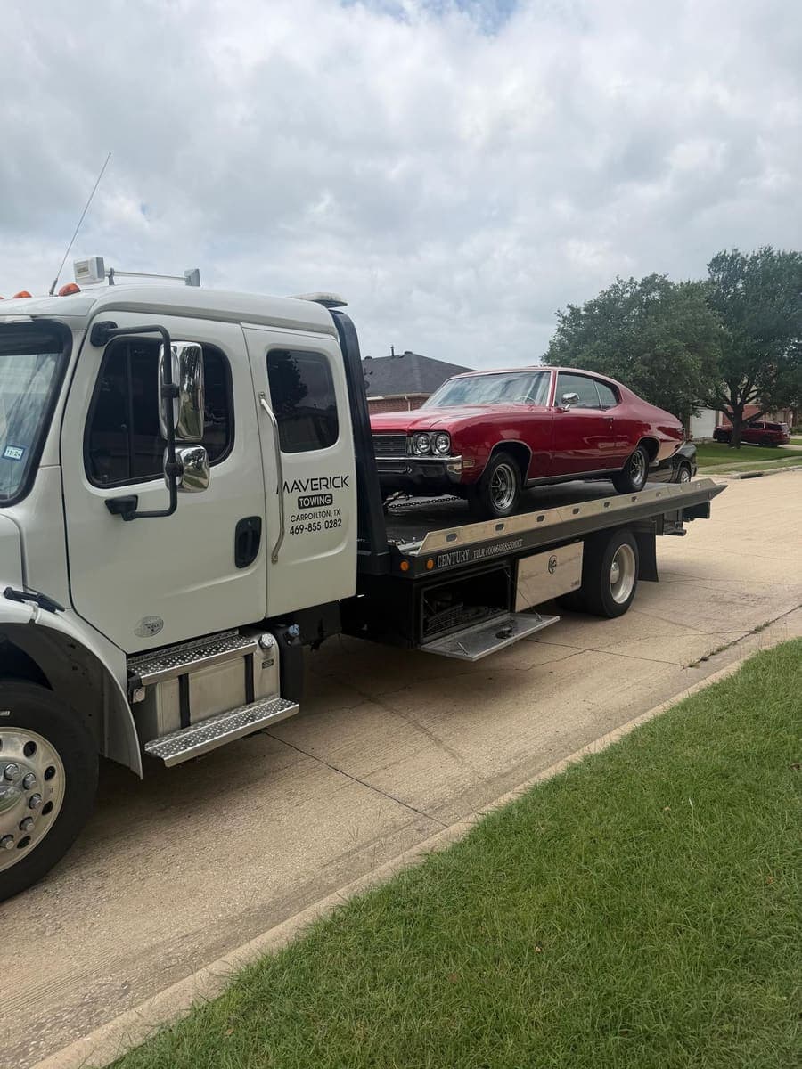 Red classic Buick coupe chained down on a Maverick Towing flatbed on a residential street