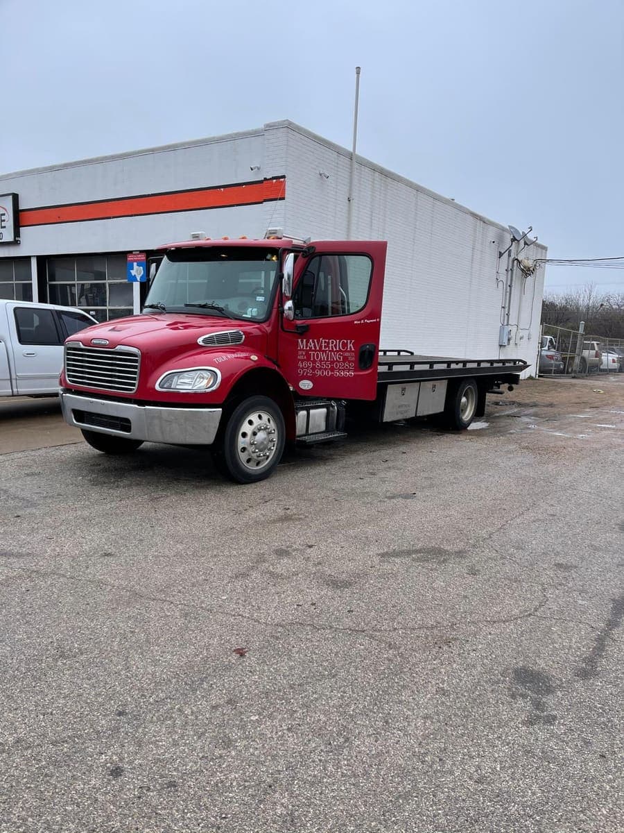Maverick Towing red Freightliner flatbed tow truck parked outside a Dallas garage
